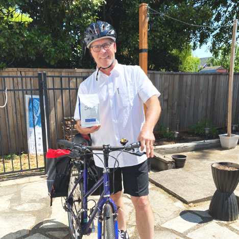 A man stands and poses with his bycicle.